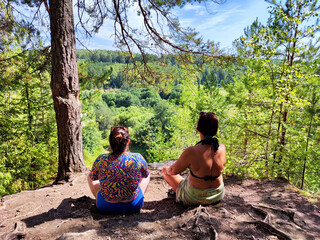 Friends relax and enjoy nature view from a ledge in a lush forest during a sunny day in summer