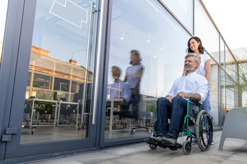 Dark-haired woman carrying a wheelchair of her husband