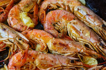 Fried Langoustines. Shrimps cooked in a frying pan with spices, herbs and lemon on a dark background. Macro shot. 