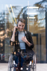 Smiling businesswoman in wheelchair using smart phone near office building