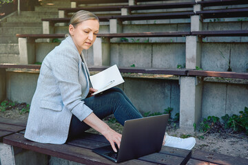 Woman working remotely on laptop with notebook outdoors. Concept of freelance, online education or...