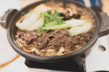 Sukiyaki meal showcasing thinly sliced beef and fresh vegetables cooking in a hot soy sauce bubbling hot pot in restaurant