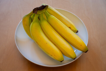 A bunch of bananas in a white dish on a wooden table