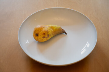 One pear lying in a white dish on a wooden table