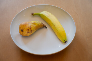 One pear and one banana in a white dish on a wooden table