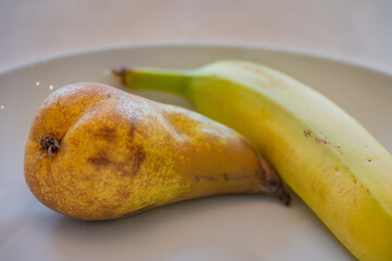 Detail view of one pear and one banana in a white dish on a wooden table