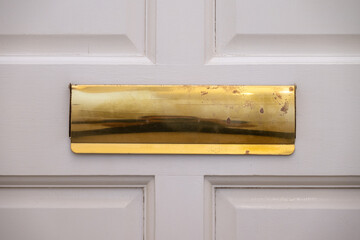 Close up of a gold-colored letter box on a white door. Old and worn.