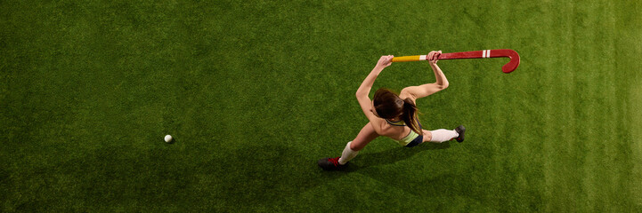Overhead photo of player swinging her stick to hit ball on green grass field against white studio background. Pure focus and energy in motion. Concept of sport events, competition, championship, game.