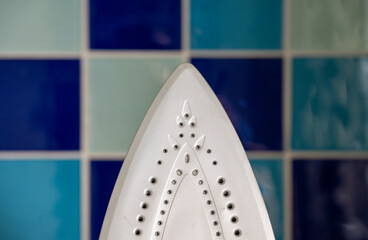 Close up of electric iron with blue tiled wall behind