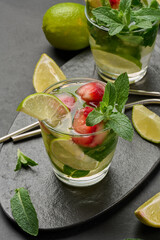 Refreshing mojito cocktail with lime, mint, strawberry, and ice on dark background