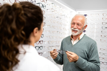 Experienced female optician recommending senior man eyeglasses to buy.