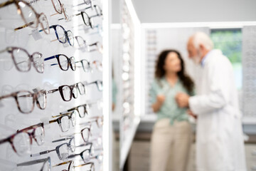 Optician store interior with many fashionable eyeglasses for sale and customer in background.