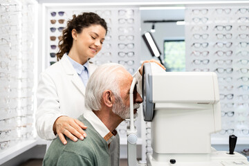 Obraz premium Experienced optometrist checking senior man eyesight focus and diopter using auto refractor optical instrument.