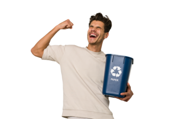 Young caucasian man holding a paper trash for recycle raising fist after a victory, winner concept.