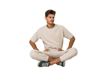 Young caucasian man sitting on the floor isolated on white background confused, feels doubtful and...