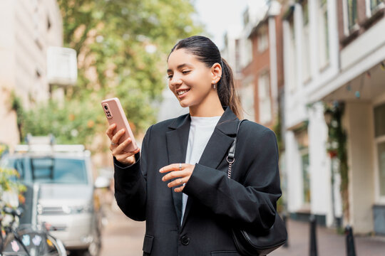 Stylish young woman exploring a new neighborhood, using her phone for local guides, mobile banking, and mindful check-ins