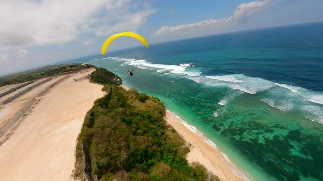 FPV drone shot of paragliders gliding over turquoise ocean and cliffs in Bali, Indonesia