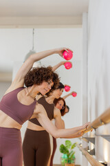 Four women leaning sideways at the barre using small pink dumbbells. Wellness, toning, strength,...