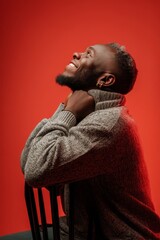 Happy young black man in grey sweater looking up and smiling with a vibrant red backdrop.
