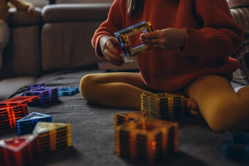 Top view of a 6-year-old girl playing with a colorful magnetic construction set at home, sitting on...