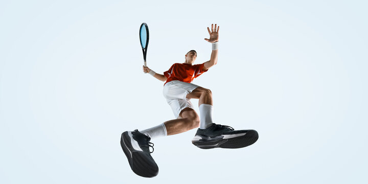 Bottom view of man, athlete jumps high with racket raised for strike wearing red shirt and white shorts against white studio background. Concept of sport, game, tournament, practice, youth