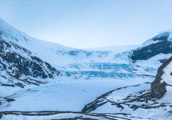 A vast, snow-covered landscape, the Athabasca Glacier, surrounded by mountains. The sky is...