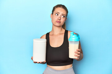 Young blonde sportswoman holding a protein shake in a studio