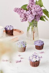 Purple aesthetics table setting - floral lilac cupcakes and coffee cup on golden tray among lilac flowers. Guilty pleasure, precious moment