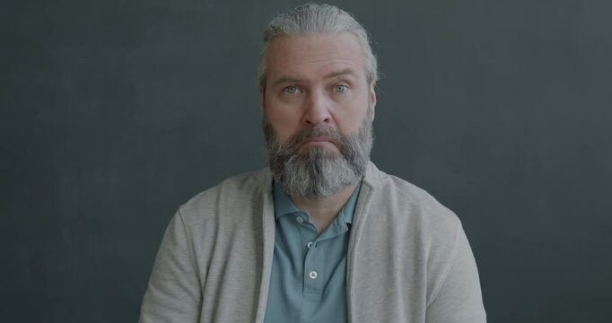Slow motion portrait of surprised and confused mature man looking at camera on gray color background. Negative emotion and people concept.