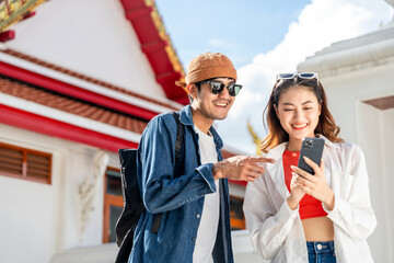 Young Asian couple man and woman traveling backpacker walking in temple at Bangkok Thailand. Happy couple tourist walking in the downtown street. Holiday vacation time tourist