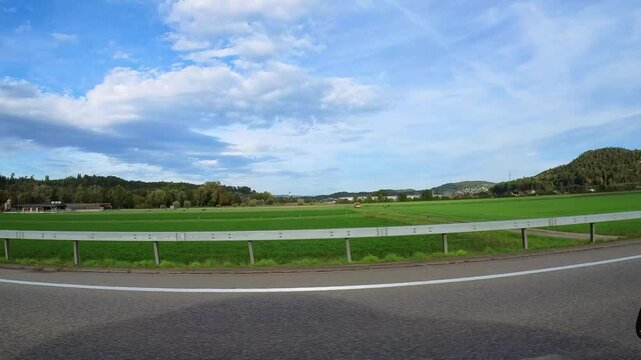 Driving backplate on a highway. View to the left, with Landscape, guardrail and oncoming traffic visible. 