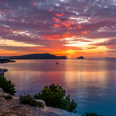 Sunrise over calm water, colorful sky, and land.