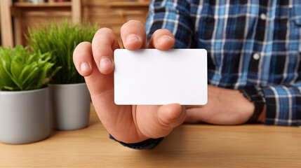 Obraz premium A man in a blue shirt is holding a blank white card in his hand while sitting at a desk indoors.