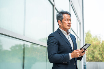 Fototapeta premium Senior manager business man in suit with tablet at the buildings downtown. Confident man using digital tablet looking towards their goals for success. Executive business man
