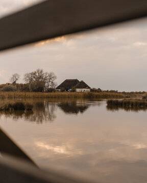 A typical "casone" with a thatched roof overlooks the calm lagoon of Marano Lagunare, in Friuli Venezia Giulia, Italy, at dusk.