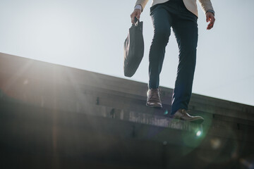 Person in formal attire descending stairs outdoors carrying a bag under sunlight.