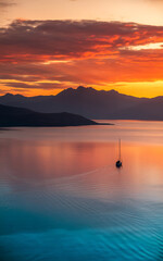 Naklejka premium Sunrise over lake, sailboat on water, mountains.