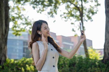 Fototapeta premium Young asian business woman with headset talking on smartphone standing in the garden public park. Cheerful woman discussion conference on smartphone