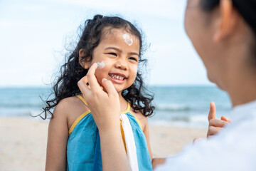 Asian mom applying sunscreen to her happy child’s face on the beach for skin protection from the...