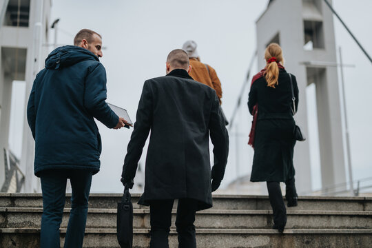 Employing a gesture of cohesion and professionalism, business colleagues ascend exterior stairs, symbolizing progress and purpose in their urban journey.