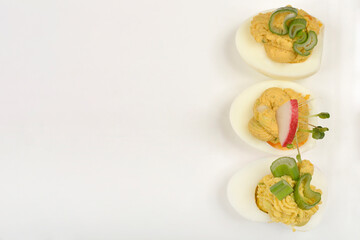 Three deviled egg halves, each uniquely garnished with celery, radish, and sprouts, are presented on a white plate