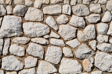 A textured stone wall is constructed from irregularly shaped, light-colored rocks and mortar