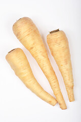 Three pale beige parsnips are arranged diagonally on a white surface