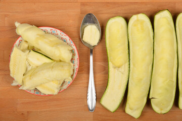 Halved and scooped-out zucchinis are arranged with removed pulp in a bowl and on a spoon on a wooden board