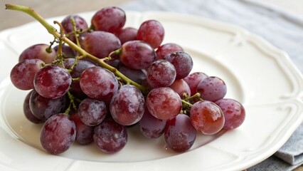 Fototapeta premium A cluster of purple grapes on a white ceramic plate.