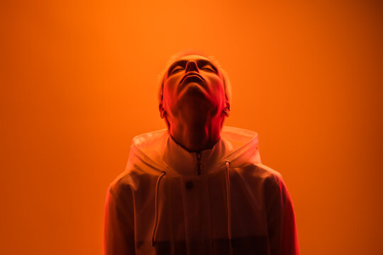 A person wearing a hoodie looks upwards, backlit in warm orange lighting. The image conveys a sense of emotion, introspection, and artistic expression, merging vibrant warm tones and dramatic