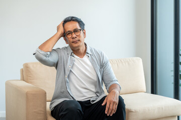 Fototapeta premium Asian mature old man sitting bored serious thinking in living room at home. Portrait of serious depressed senior asian man. Mature People with problem in life