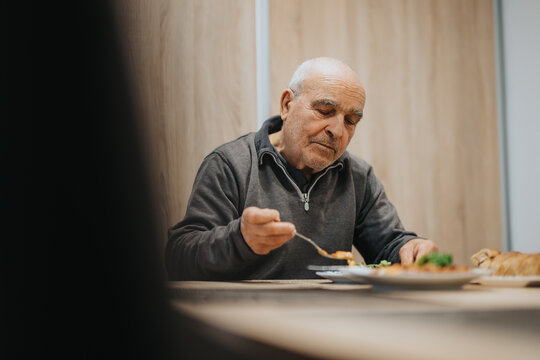 An elderly man eating a quiet meal at home, showcasing a serene moment during his day. Captures the simplicity and routine of everyday life in a warm indoor setting.