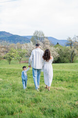 Young beautiful family walking in a field with blooming cherry trees. Dad, mom and little son playing in the garden outdoors.
