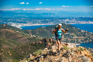 Fototapeta premium Female hiker hiking the impressive red mountain of Cap Roux at the Massif de L'Esterel on the Mediterranean coast in the French Riviera